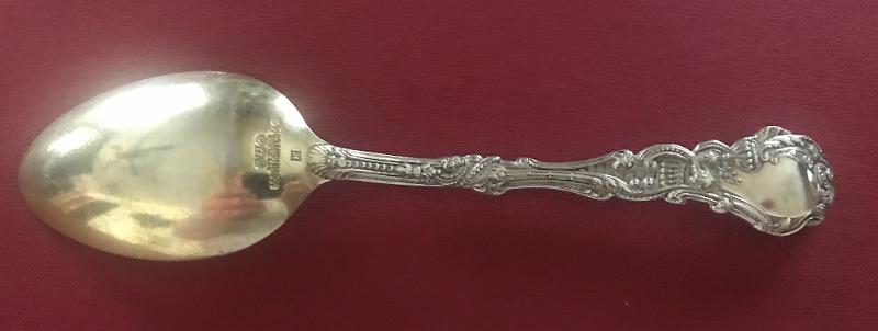 Souvenir Mining Spoon Reverse Oronogo No. 1 Mine, Oronogo, Jasper Co.,  MO.JPG - SOUVENIR MINING SPOON ORONOGO MINE NO 1 ORONOGO MO [Sterling silver spoon, 5 7/8 in. long, engraved mining scene in bowl, bowl marked OROGONO NO. 1, handle front in ornate Versailles pattern introduced in 1888 by Gorham;  It shows an angel holding a musical instrument, maybe pipes or a lyre; reverse is marked with the old lion-anchor-G  hallmark for Gorham, K in a square shape and Sterling; weight 30.9 gms. [Eight miles north of Joplin, Missouri stands the village of Oronogo, originally named Minersville when it sprang up in 1850. According to legend, a miner dug there with his pick and shovel and said, "It's ore here or no go," and so the name Oronogo stuck. Nearby is the site of the richest lead and zinc strike ever made in southwest Missouri. Tom Livingston first discovered the mine before the Civil War, but renegades stole his land while he was away fighting. After the war, they sold it to Granby Mining Company for $50. After almost 80 years of continuous operation, the mine produced $30 million worth of lead and zinc. The Oronogo Circle Mine No. 1, one of the few open-pit mines in the district, stretched 300 feet deep and 600 feet across. The 12-acre unroofed cavern was strip mined at three levels-150 feet, 240 feet, and 360 feet--a flurry of activity with men, trucks, and machinery going up and down the steep inclines. Numerous mills serviced the operation. The largest chunk of pure lead ever found in the district came from the Oronogo Circle. Two flat cars carried it to the World's Fair in Chicago in 1893. After the exhibit ended, the mammoth rock sold for $6,000. A deadly accident occurred at the mine in 1901 when a blast of dynamite detonated prematurely, killing 12 men and wrecking a $50,000 mill. Operations shut down for several months because miners refused to go back to work. Chicago capitalists ran the mine from 1906 to 1914, raking in profits of $3 million. They sold it to the Connecticut Mining Company for $500,000. The ground was so honeycombed with shafts and drifts at four levels that it was no longer safe to work underground. In an ill-fated endeavor to make mining the Circle safer, the new owners closed the old shafts and dismantled 20 small mills. They removed underground support pillars and stripped the entire tract down to 300 feet, using the largest steam shovels available. Then they buried dynamite at the former mill sites and ignited them all at once, causing a blast that almost blew Oronogo off the map. The ground shook so violently that a new mill, built on solid ground, fell into the pit and killed six men. The catastrophe cost the company more than $1 million. Connecticut Mining went out of business, and the mine reverted to its original owner, the Granby Mining Company. For many years, the tract lay idle, although investors made half-hearted attempts to resume strip mining. By the 1970s, the huge water-filled pit had become popular with scuba divers, who liked to explore its depths, yet even that turned out tragically, with the deaths of some of the divers.]